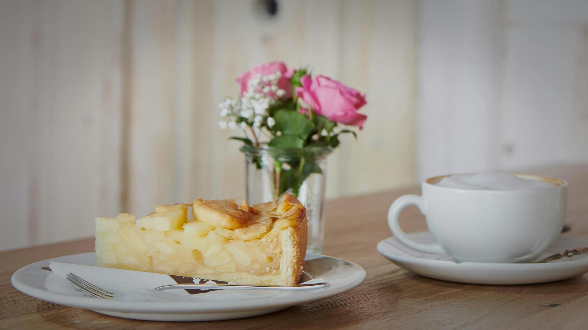 Stück Apfelkuchen neben einer gefüllten Cappuccino Tasse
